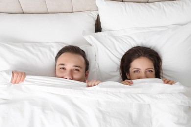 Lovely couple hiding under blanket in bed, top view