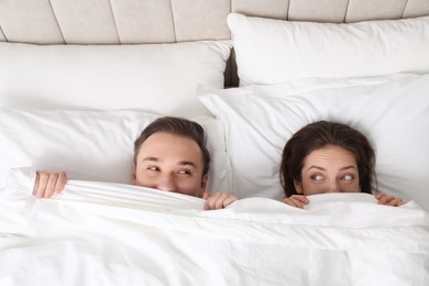 Photo of Lovely couple hiding under blanket in bed, top view