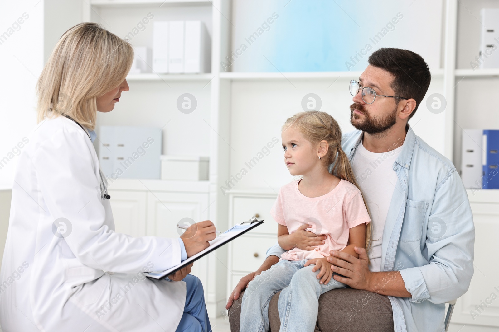 Photo of Doctor consulting little girl with stomach pain and her father in hospital