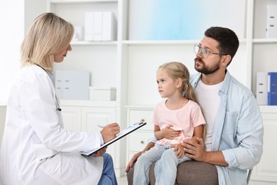 Photo of Doctor consulting little girl with stomach pain and her father in hospital