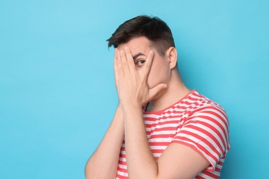 Portrait of scared young man on light blue background, space for text