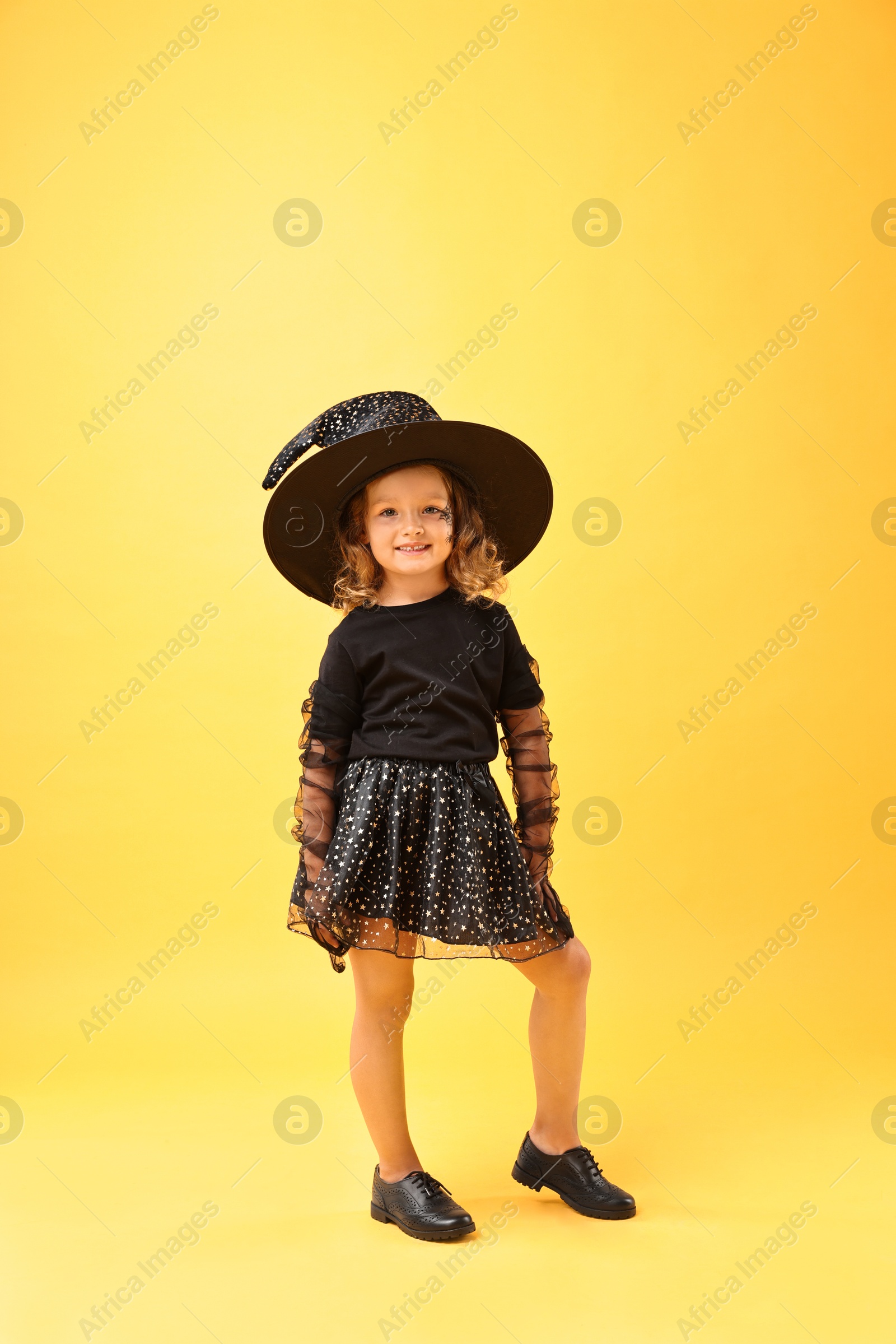 Photo of Cute girl dressed like witch on yellow background. Halloween costume