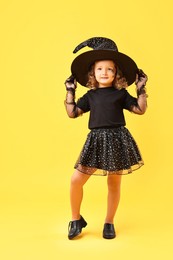 Photo of Cute girl dressed like witch on yellow background. Halloween costume