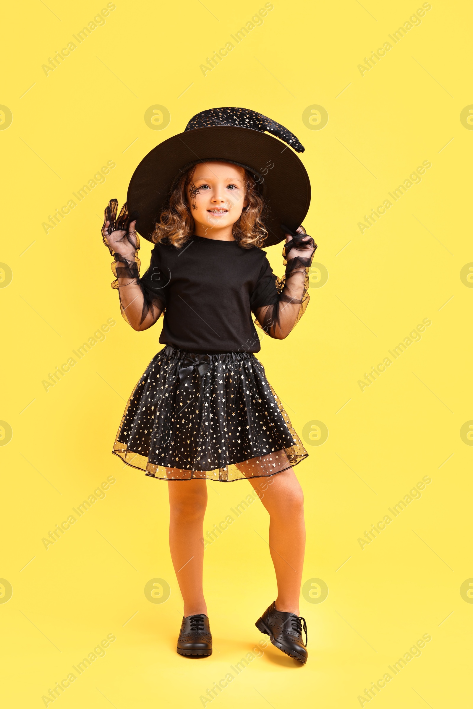 Photo of Cute girl dressed like witch on yellow background. Halloween costume