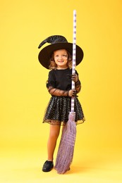 Cute girl with broom dressed like witch on yellow background. Halloween celebration