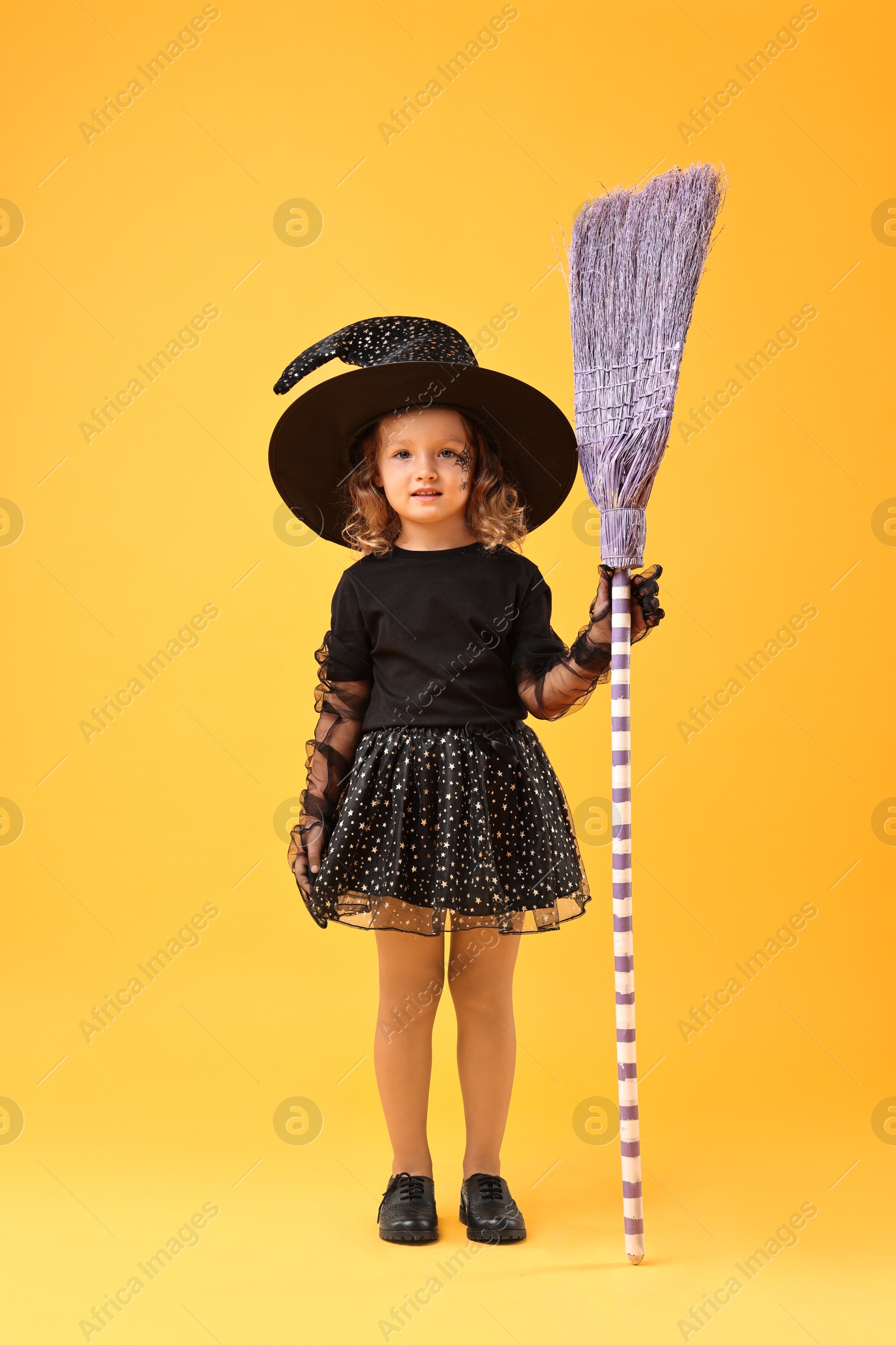 Photo of Cute girl with broom dressed like witch on yellow background. Halloween celebration