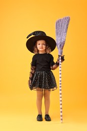 Photo of Cute girl with broom dressed like witch on yellow background. Halloween celebration