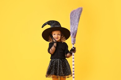 Photo of Cute girl with broom dressed like witch on yellow background. Halloween celebration