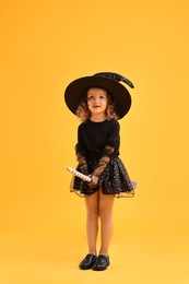 Photo of Cute girl with broom dressed like witch on yellow background. Halloween celebration