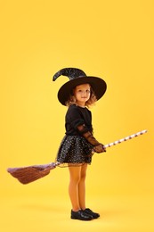 Photo of Cute girl with broom dressed like witch on yellow background. Halloween celebration