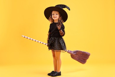 Photo of Cute girl with broom dressed like witch on yellow background. Halloween celebration