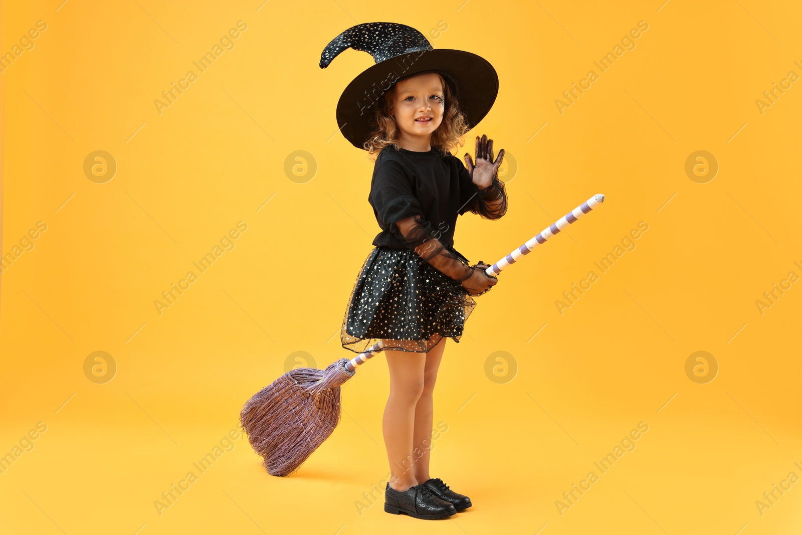 Photo of Cute girl with broom dressed like witch on yellow background. Halloween celebration