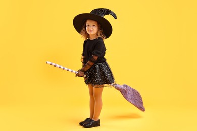 Photo of Cute girl with broom dressed like witch on yellow background. Halloween celebration