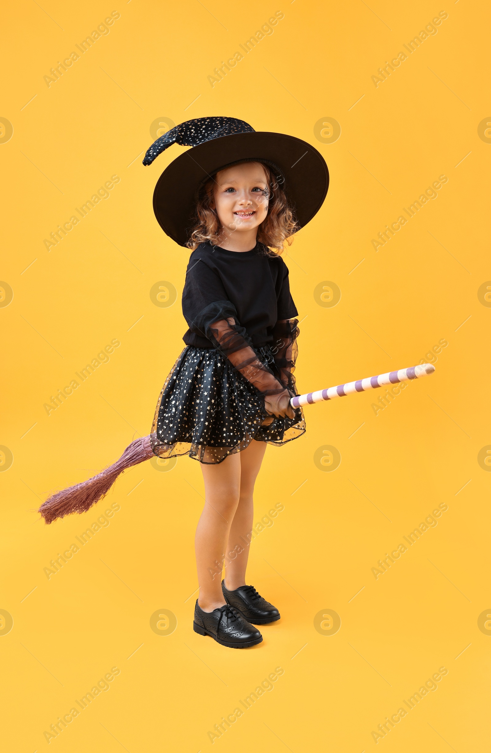 Photo of Cute girl with broom dressed like witch on yellow background. Halloween celebration