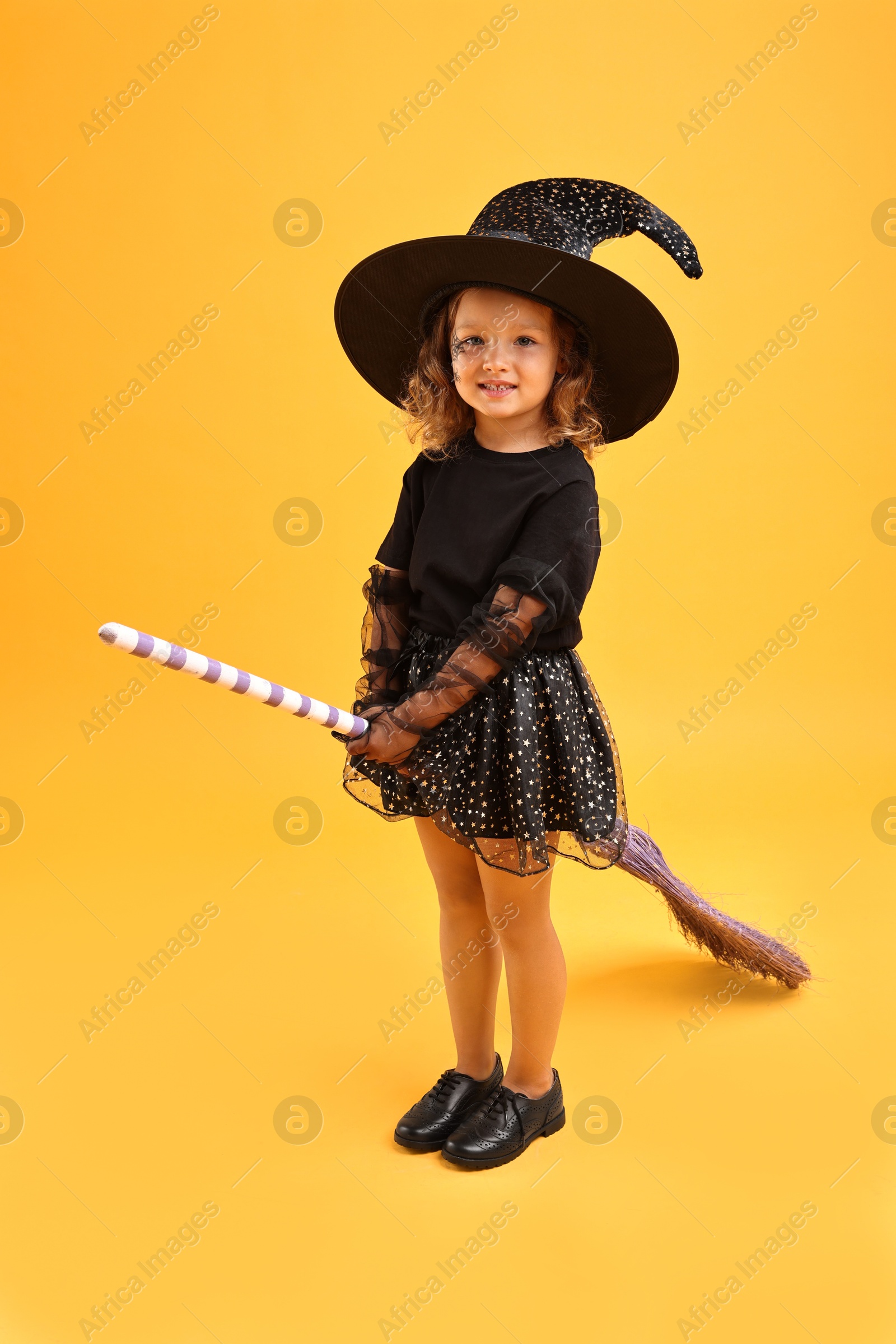 Photo of Cute girl with broom dressed like witch on yellow background. Halloween celebration