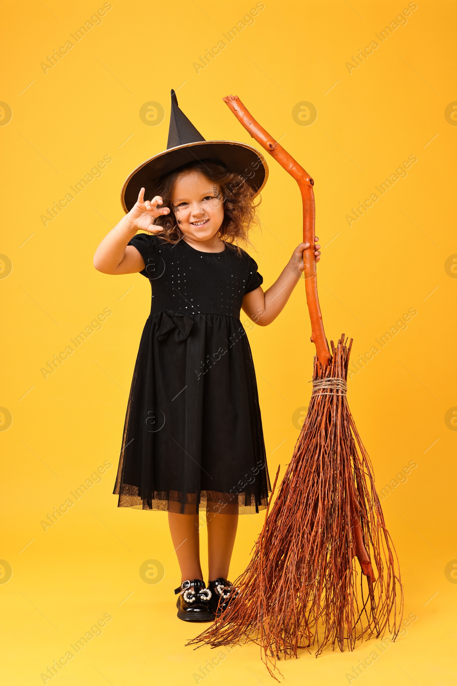 Photo of Funny girl with broom dressed like witch on yellow background. Halloween celebration