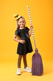 Funny girl with broom dressed like witch on yellow background. Halloween celebration