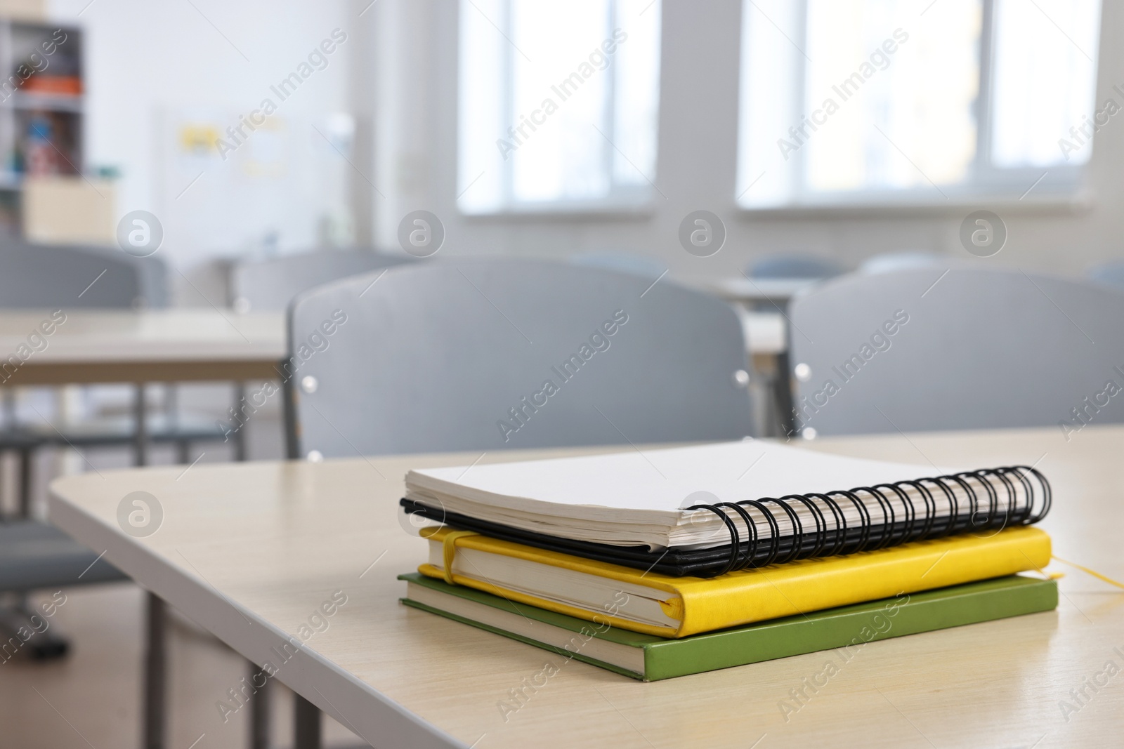 Photo of Stack of notebooks on wooden desk in empty classroom