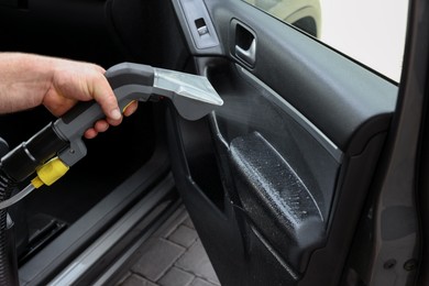 Photo of Man cleaning car door with vacuum cleaner, closeup