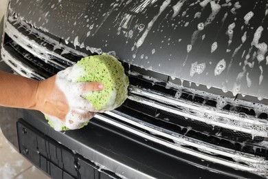 Photo of Man washing car hood with sponge indoors, closeup