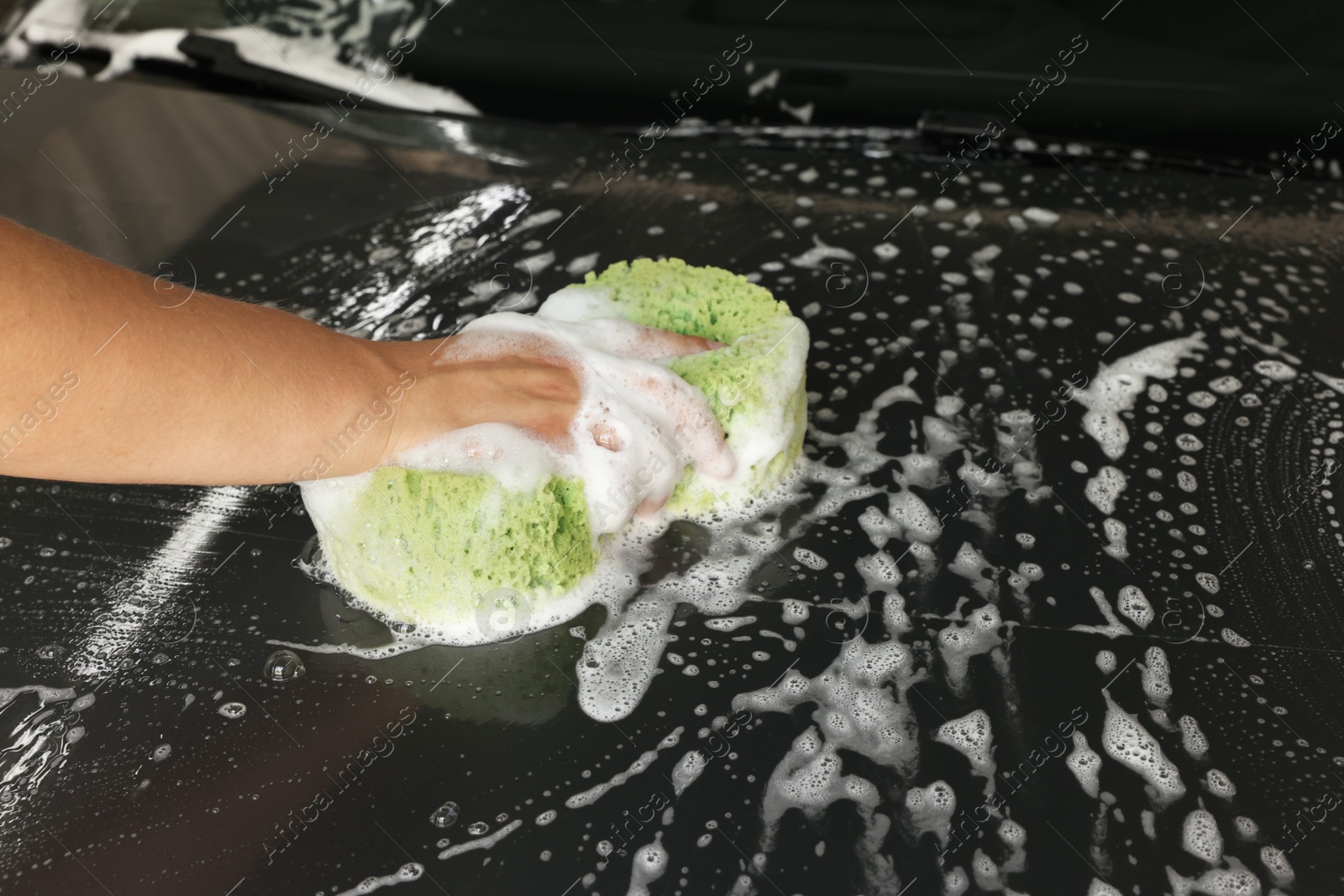 Photo of Man washing car hood with sponge indoors, closeup