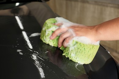 Man washing car hood with sponge indoors, closeup