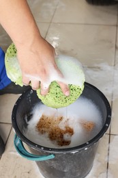 Photo of Man holding sponge with foam near basket at car wash, closeup