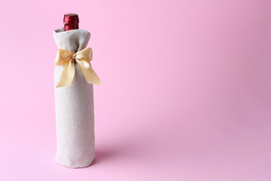 Photo of Wine bottle in burlap bag with satin bow on pink background. Space for text