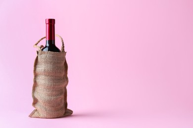 Wine bottle in burlap bag on pink background. Space for text