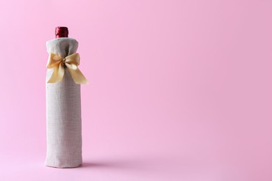 Photo of Wine bottle in burlap bag with satin bow on pink background. Space for text