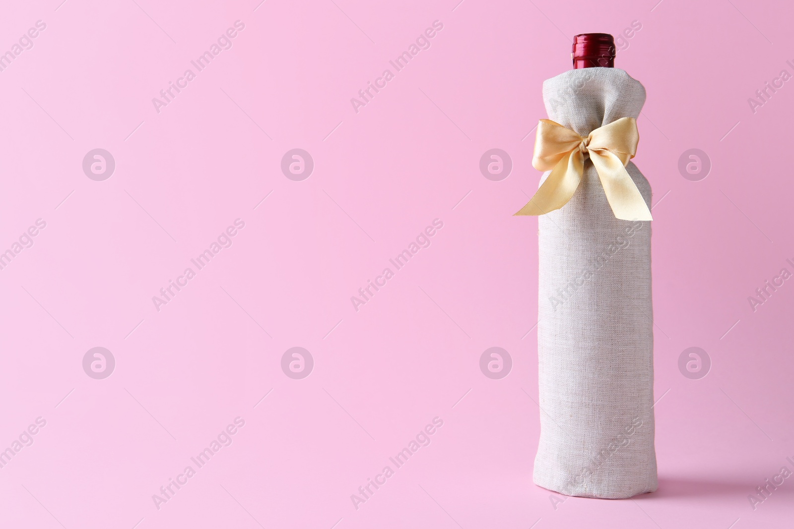 Photo of Wine bottle in burlap bag with satin bow on pink background. Space for text