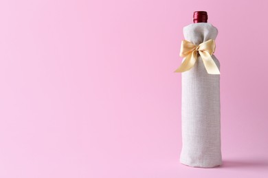 Photo of Wine bottle in burlap bag with satin bow on pink background. Space for text