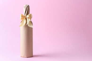 Photo of Wine bottle in burlap bag with satin bow on pink background. Space for text