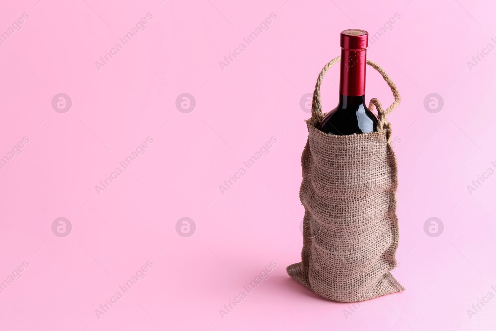 Photo of Wine bottle in burlap bag on pink background. Space for text