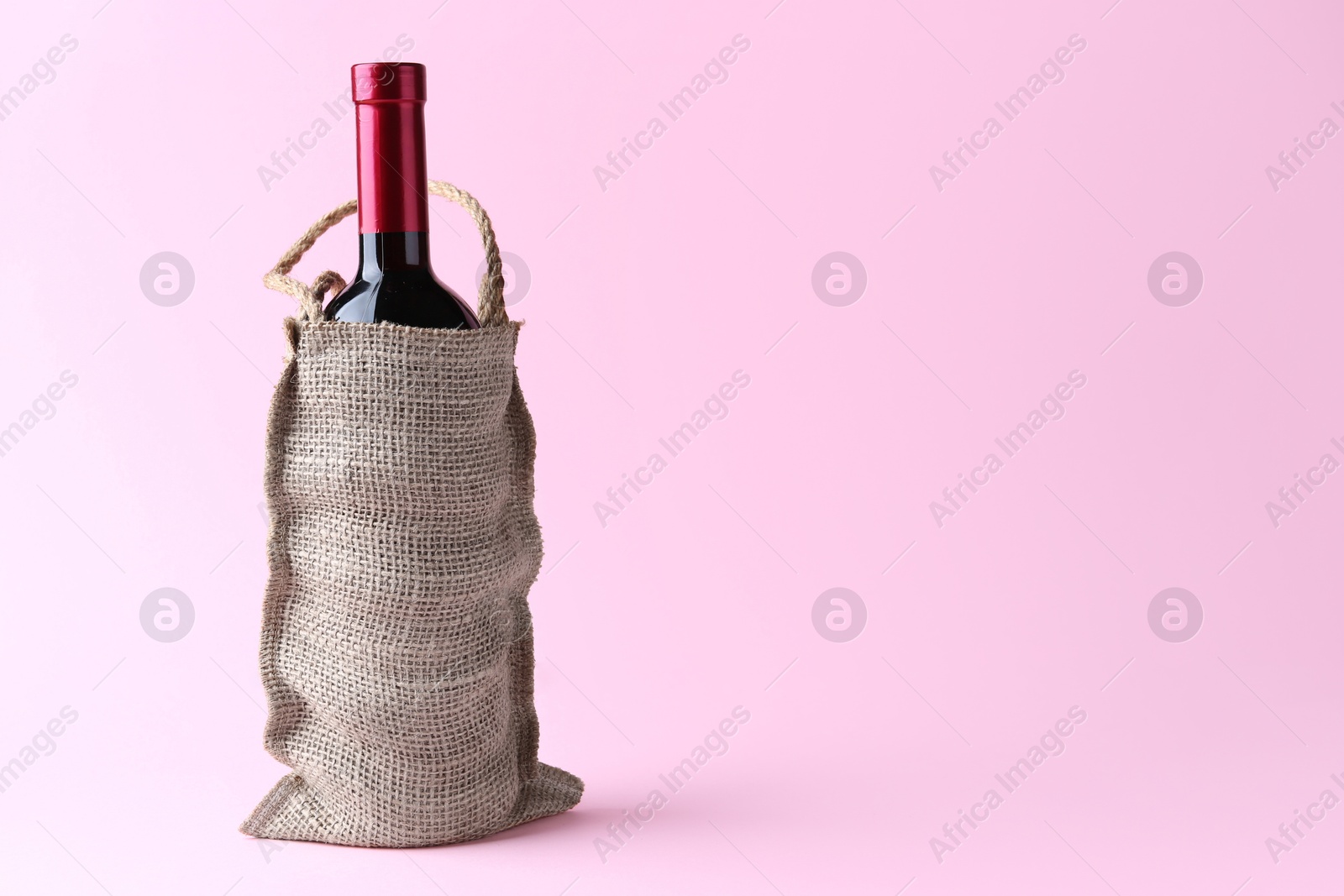 Photo of Wine bottle in burlap bag on pink background. Space for text