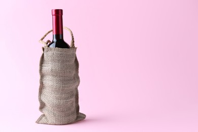 Wine bottle in burlap bag on pink background. Space for text