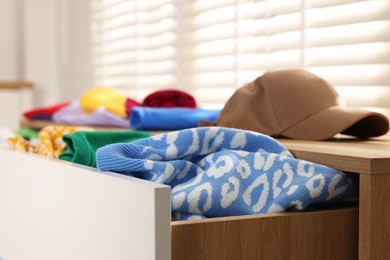 Cluttered chest of drawers indoors, closeup. Clothes in mess