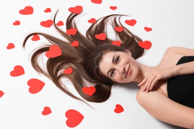 Beautiful young woman with long hair and red paper hearts on white background