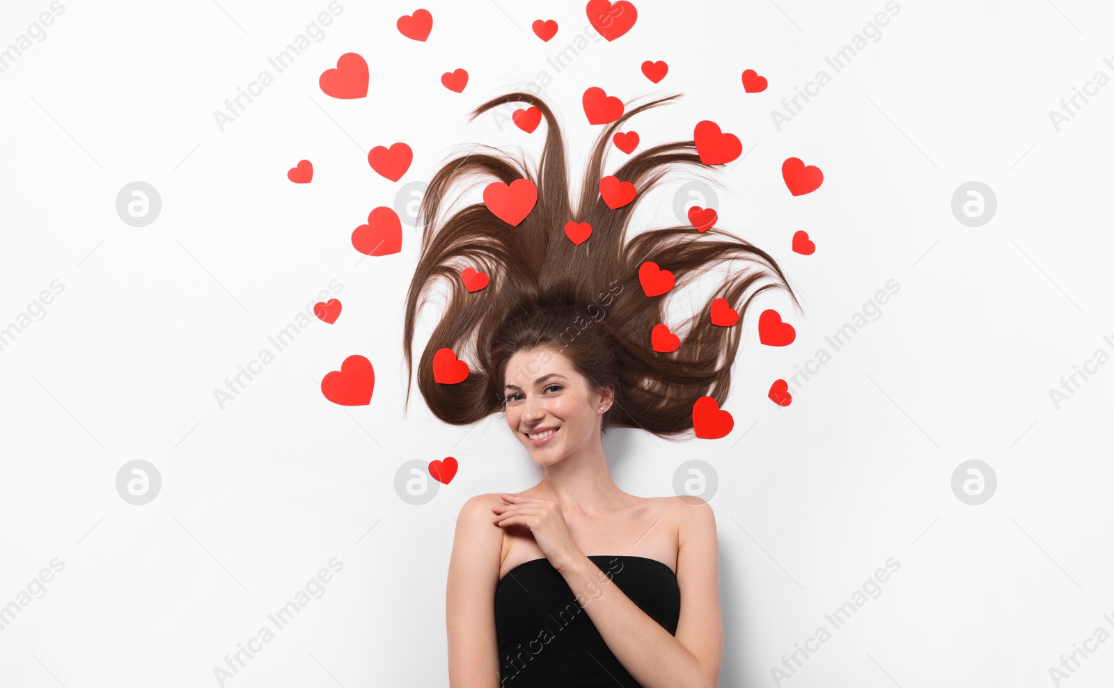 Photo of Beautiful young woman with long hair and red paper hearts on white background, top view