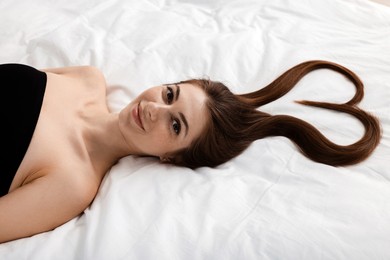 Photo of Beautiful young woman with hair in shape of heart on bed