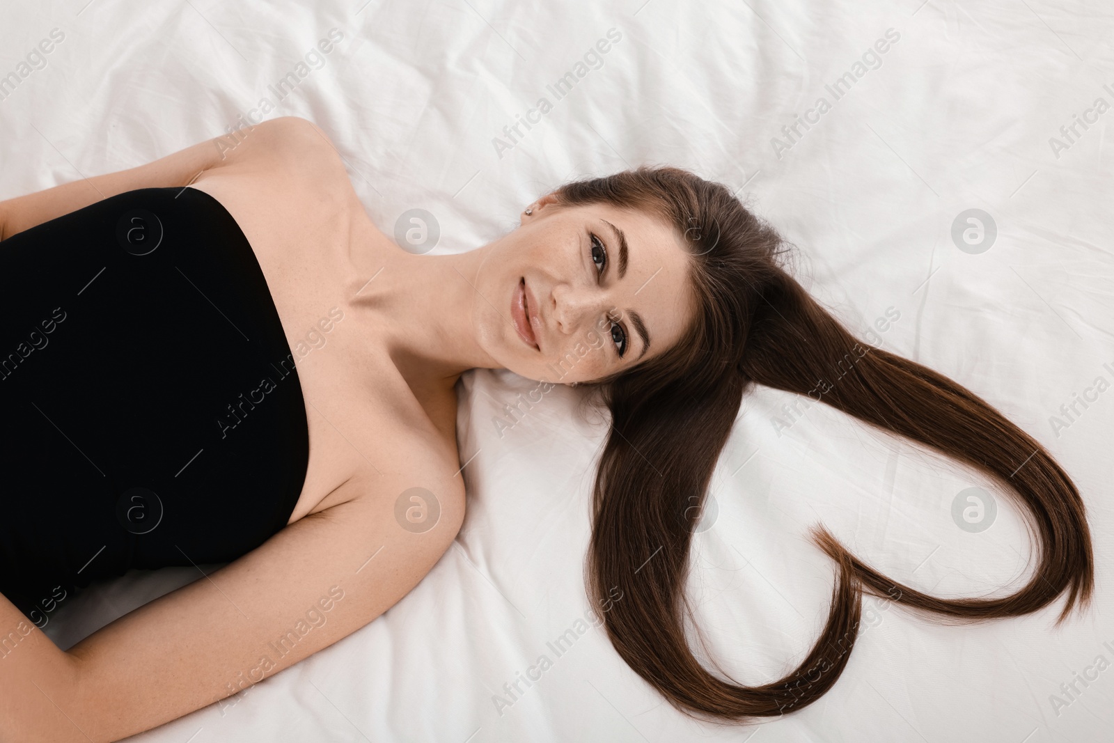 Photo of Beautiful young woman with hair in shape of heart on bed, top view