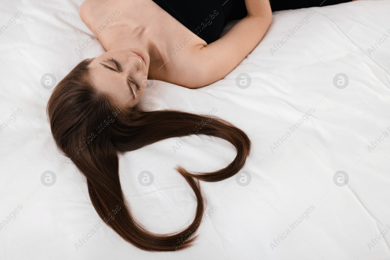 Photo of Beautiful young woman with hair in shape of heart on bed