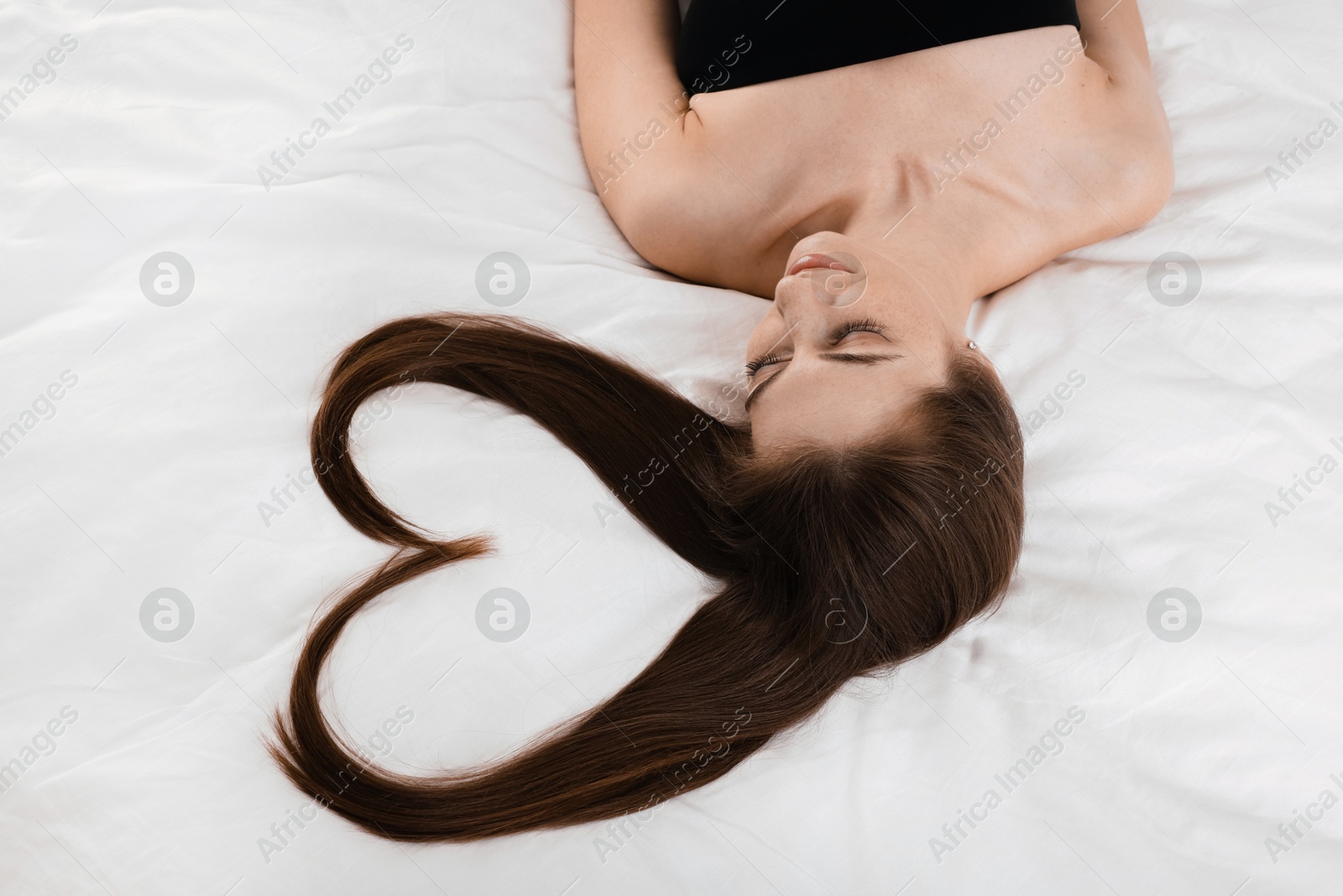 Photo of Beautiful young woman with hair in shape of heart on bed