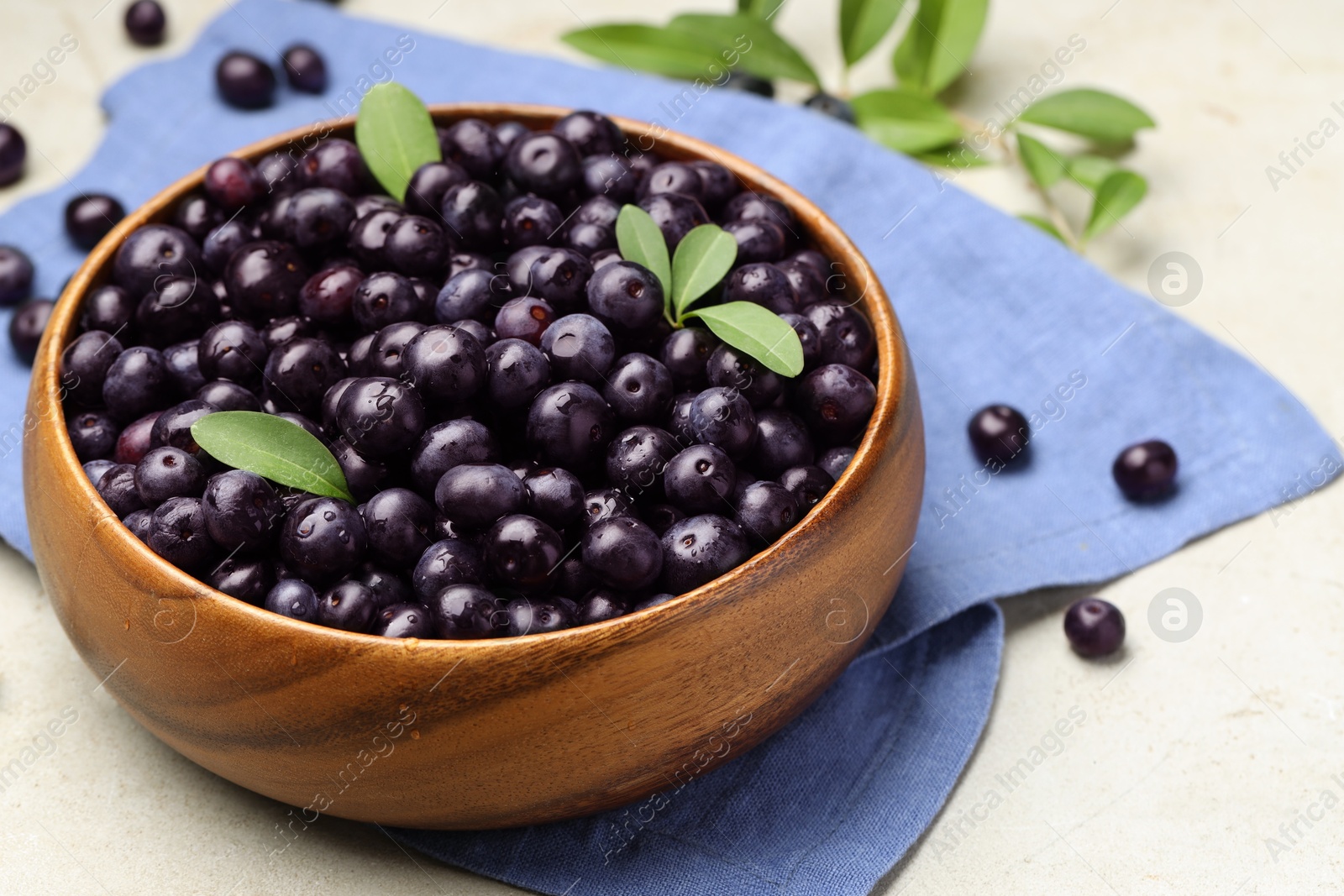 Photo of Ripe acai berries and leaves in bowl on grey table, closeup