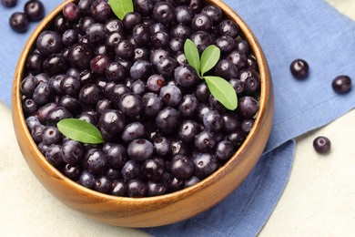 Photo of Ripe acai berries and leaves in bowl on table, above view