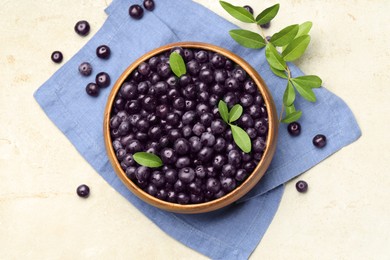 Photo of Ripe acai berries and leaves in bowl on light table, flat lay