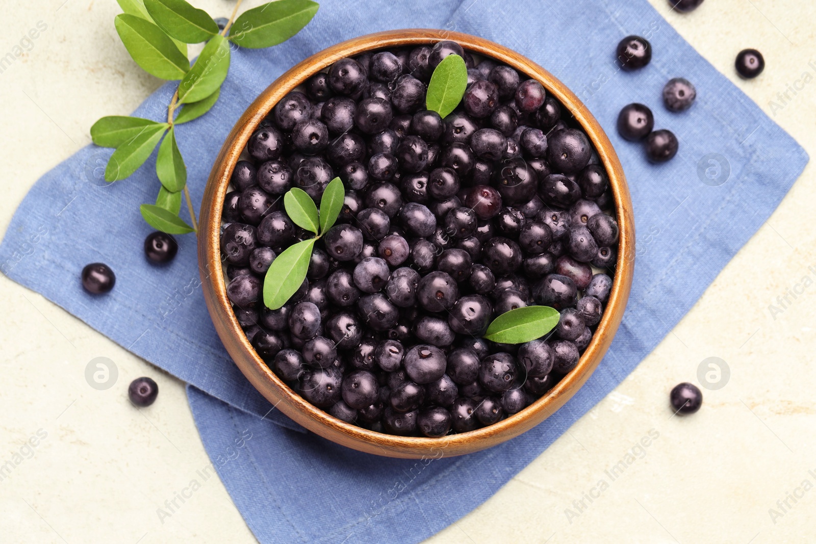 Photo of Ripe acai berries and leaves in bowl on light table, flat lay