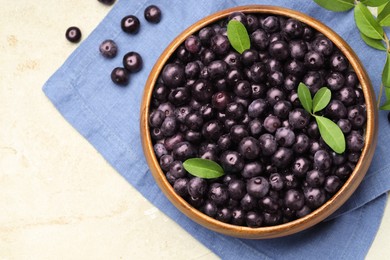 Ripe acai berries and leaves in bowl on light table, flat lay. Space for text