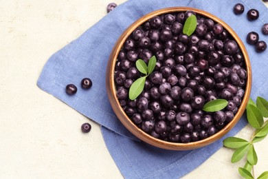 Photo of Ripe acai berries and leaves in bowl on light table, flat lay. Space for text