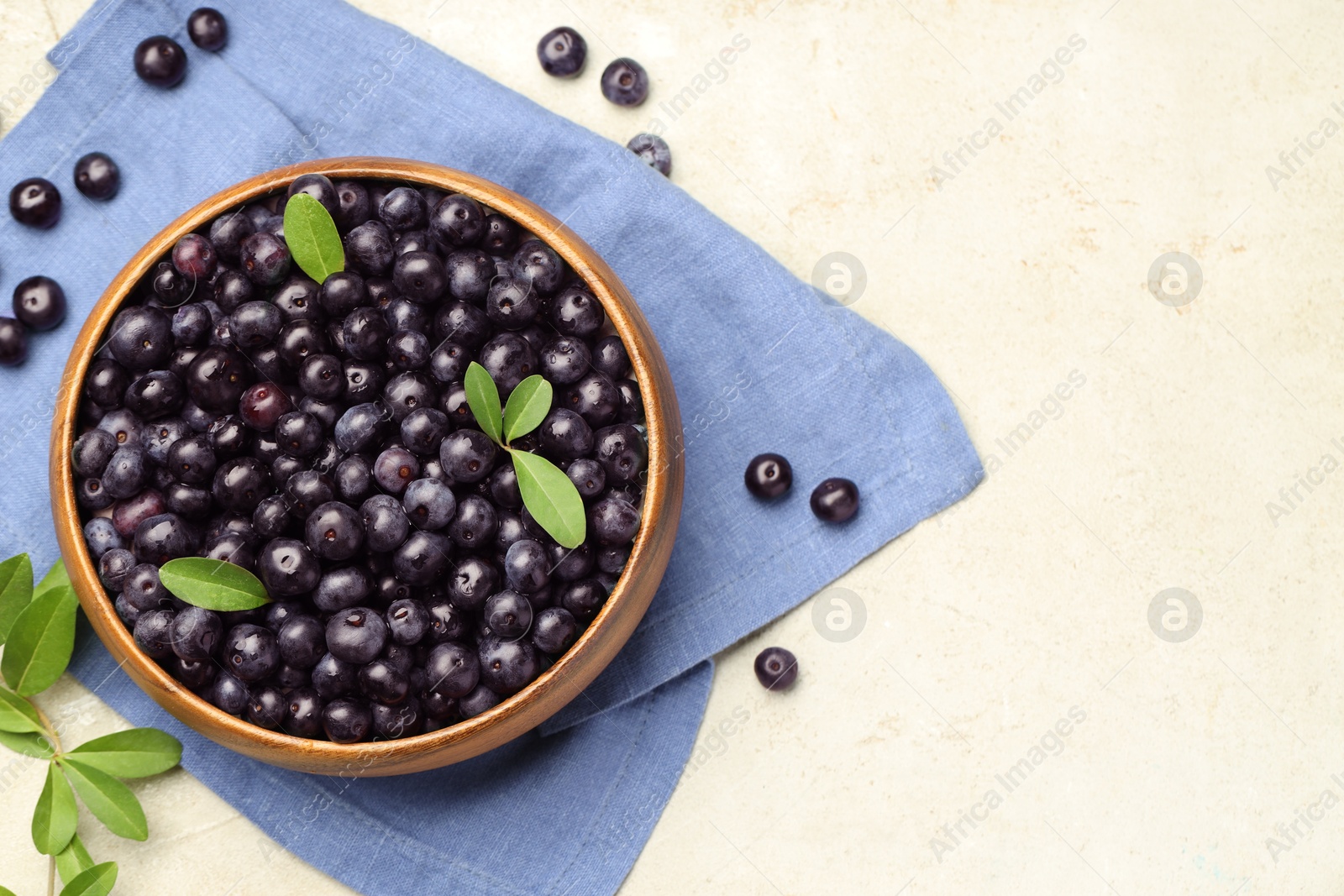 Photo of Ripe acai berries and leaves in bowl on light table, flat lay. Space for text